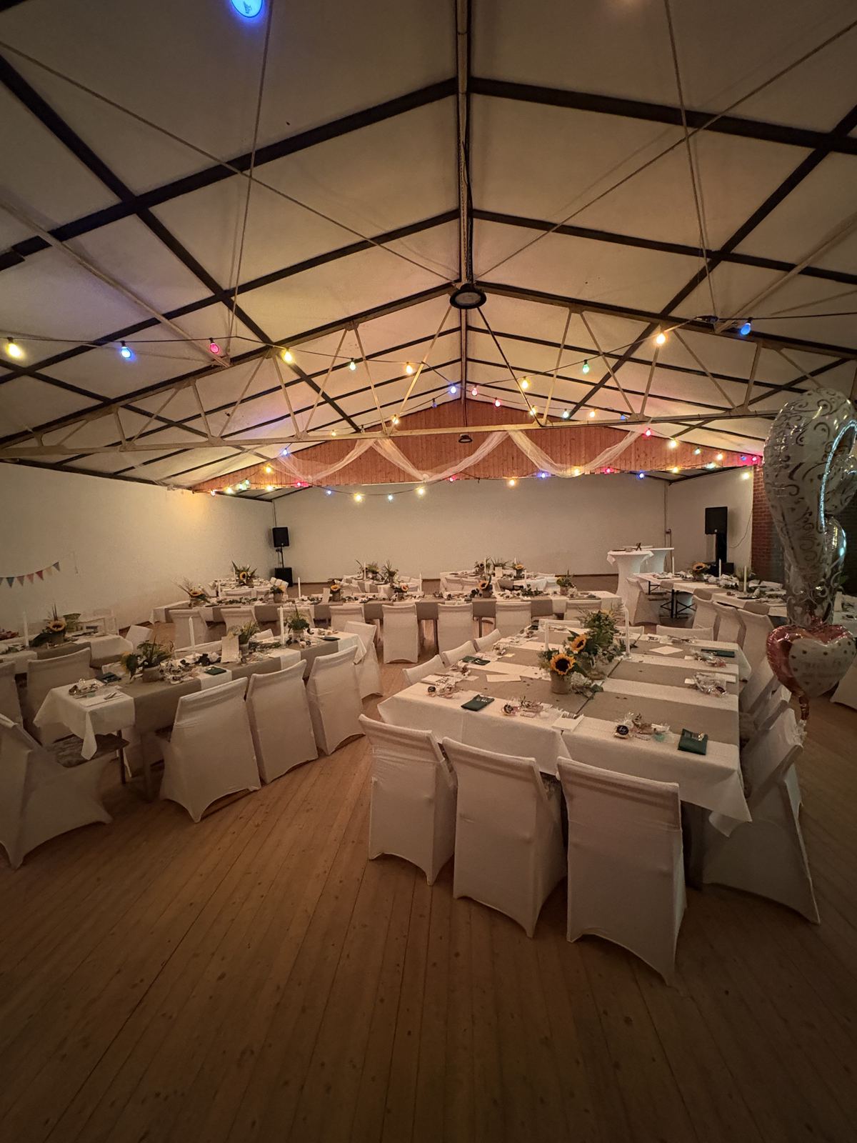 Blick über den gesamten Festsaal mit gedeckten Tafeln und Lichterketten unter dem Dach